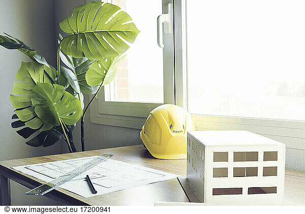 Architectural model with paper and hardhat on desk against window in office