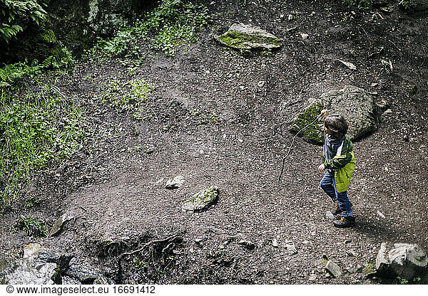 Area view boy walking stick over mud by rocks and grass