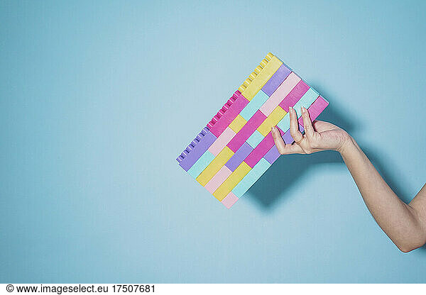 Arm of woman holding colorful pastel colored toy blocks against blue background