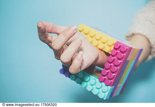 Arm of woman wearing colorful cube made of pastel colored toy blocks as bracelet
