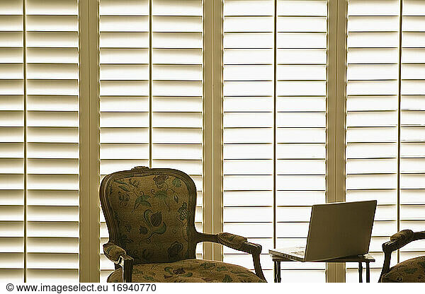 Armchair and laptop in front of domestic wooden window shutters.