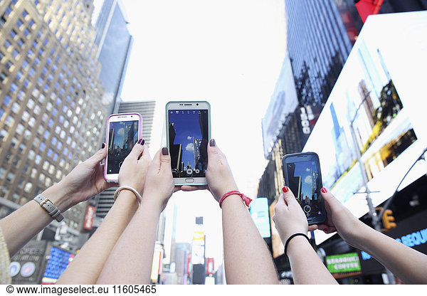 Arms of Caucasian women photographing skyscrapers with cell phones