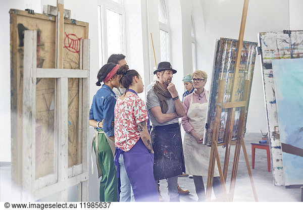 Art students and instructor examining  critiquing painting in art class studio