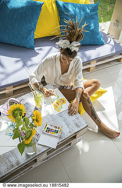 Artist painting flower on paper sitting at home