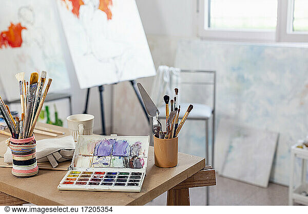 Artist's canvas and variety of paintbrush on table at home studio