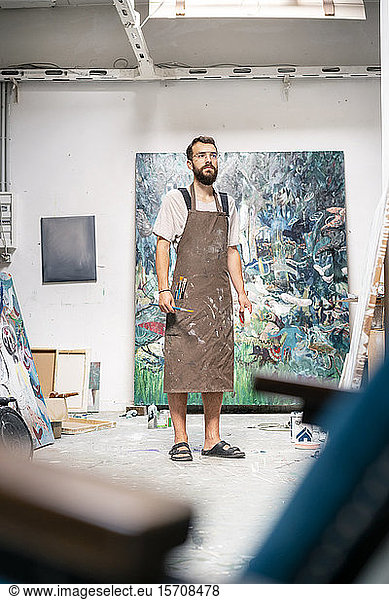 Artist standing in his studio  holding paint brush
