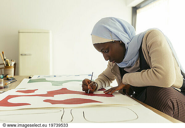 Artist wearing headscarf painting with brush in studio