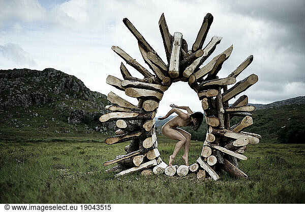 Artistic nude woman dancer balances in wooden sculpture in mountains