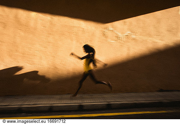 Artistic speed blur of young woman running against yellow wall