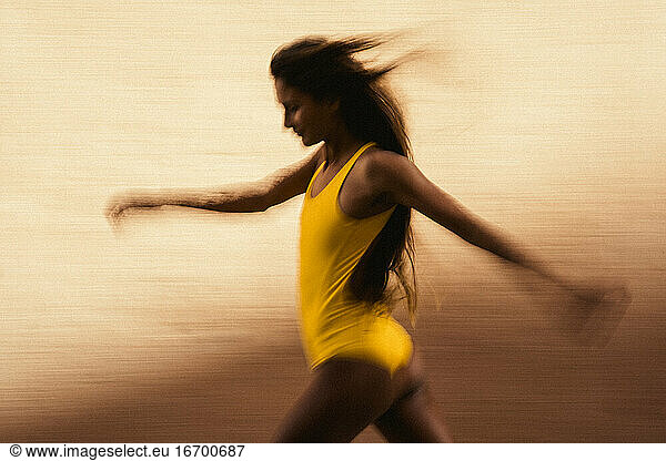Artistic speed blur of young woman running against yellow wall