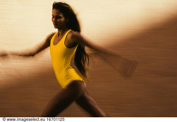 Artistic speed blur of young woman running against yellow wall