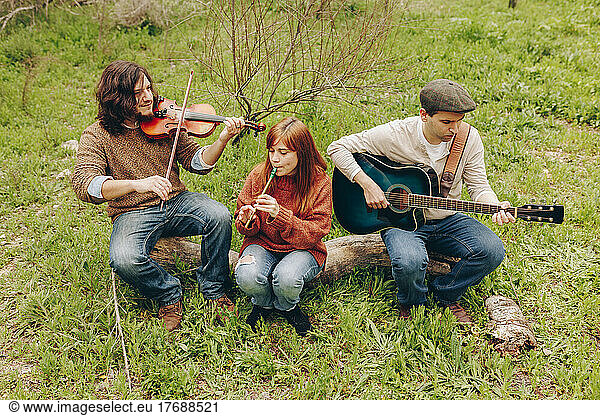 Artists practicing musical instruments sitting on log in field