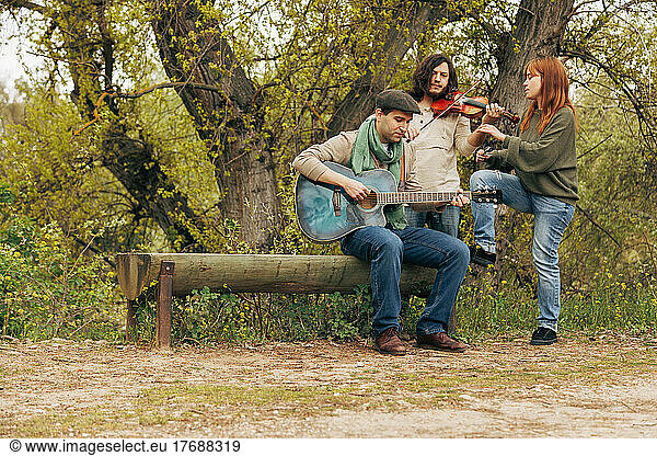 Artists with musical instruments practicing near bench by tree