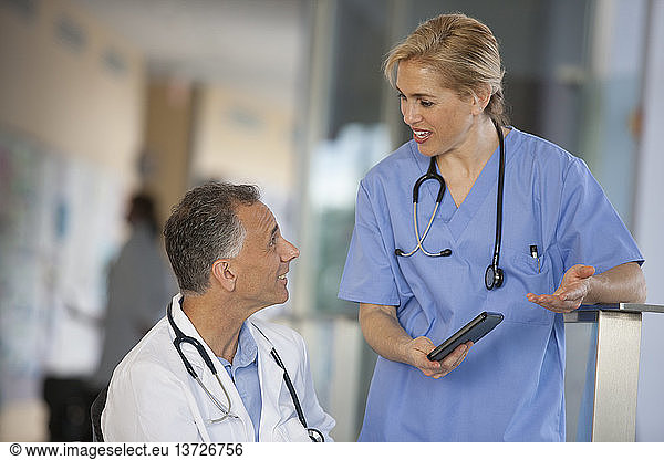 Arzt im Rollstuhl mit Rückenmarksverletzung im Gespräch mit Krankenschwester über Informationen auf Tablet