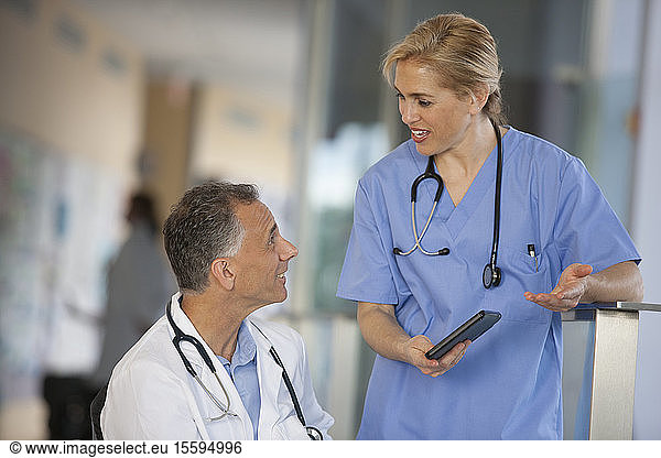 Arzt im Rollstuhl mit Rückenmarksverletzung im Gespräch mit Krankenschwester über Informationen auf Tablet