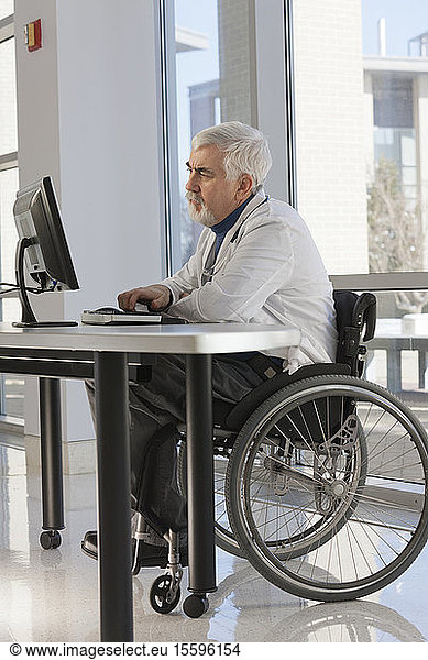 Arzt mit Muskeldystrophie im Rollstuhl studiert Informationen auf seinem Computer