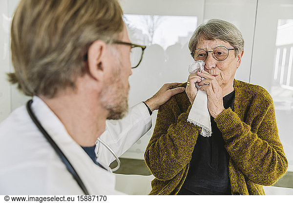 Arzt tröstet traurigen älteren Patienten in medizinischer Praxis