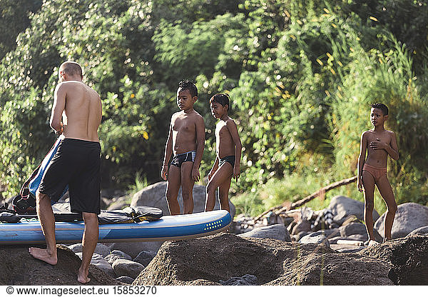 Asian boys looking at surfboard near river