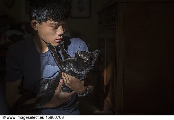 Asian Chinese boy holds black cat who touches the boy's face with paws