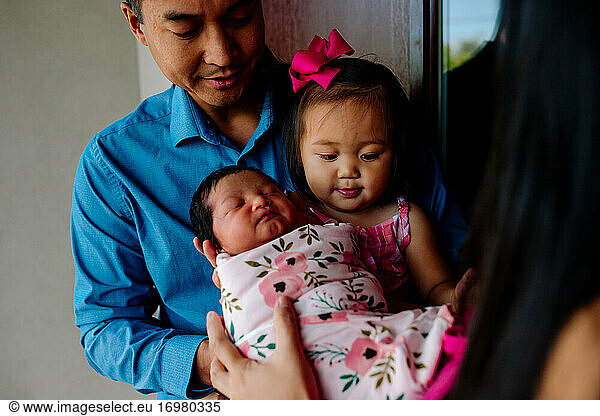 Asian dad helps young daughter hold newborn sister