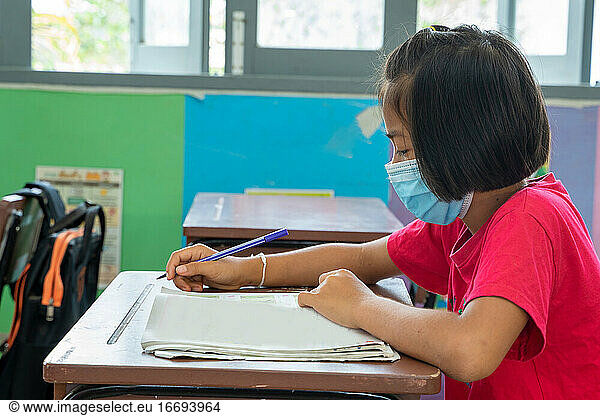 Asian elementary school wear mask for protect corona virus desk