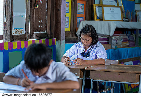 Asian elementary students in uniform studying together at classr