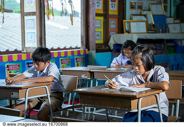 Asian elementary students in uniform studying together at classr