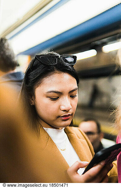 Asian girl on the subway using the phone surrounded by people
