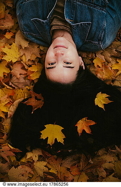 Asian Japanese young woman in jean jacket lays in fall leaves