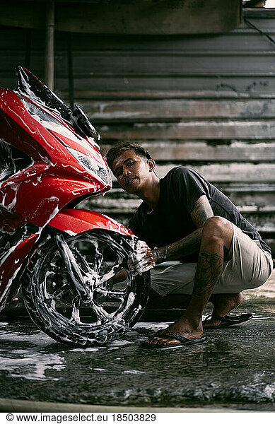 Asian man washing motorbike with soap at service station.