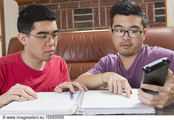 Asian man with Autism working on his homework with his brother on a phone