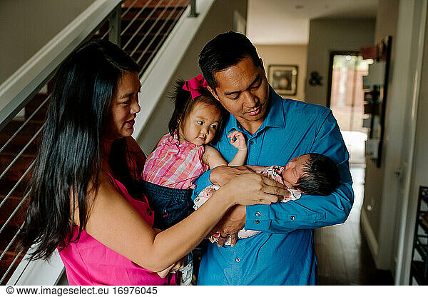 Asian mom and dad hold young daughter and newborn baby