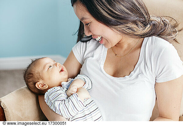 Asian mother holding rocking newborn infant baby son. Home lifestyle
