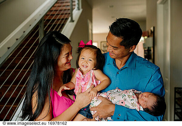 Asian parents laugh with young daughter while holding newborn