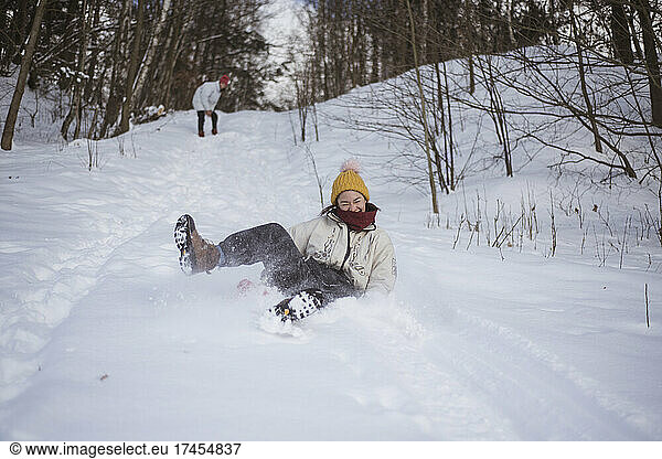 asian person laughs with joy sledging down snow hill on toboggan