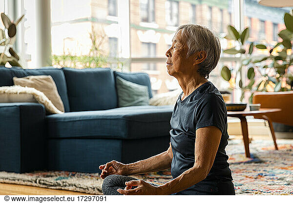Asian senior woman meditating and relaxing at home in living room