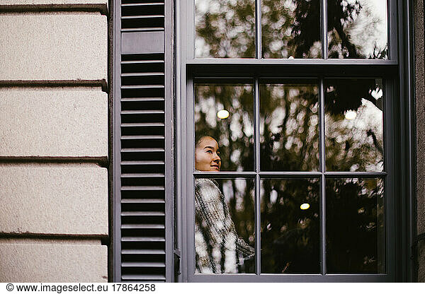 Asian woman gazes contentedly outside window from comfortable house