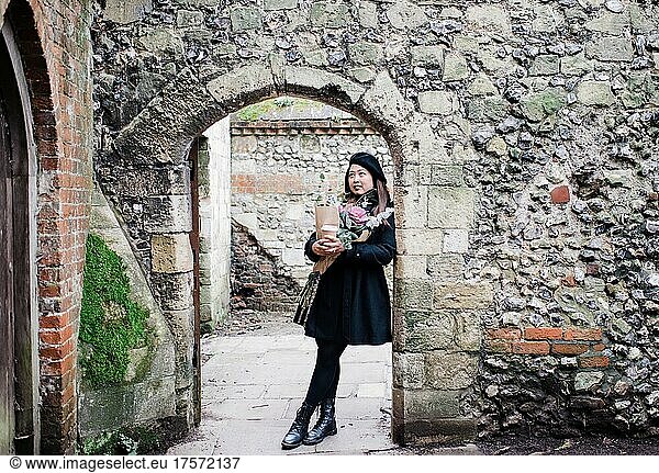 Asian woman leaning against historic wall in England
