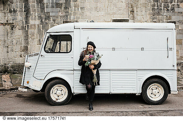 Asian woman leaning on a truck holding flowers and coffee