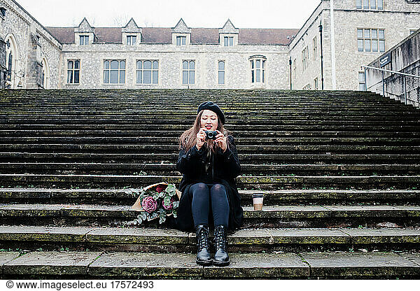Asian woman sat on steps taking pictures in Winchester  UK