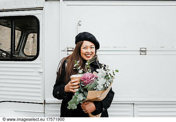 asian woman smiling holding flowers and takeaway coffee