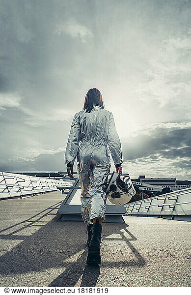 Astronaut wearing space suit holding helmet walking on footpath
