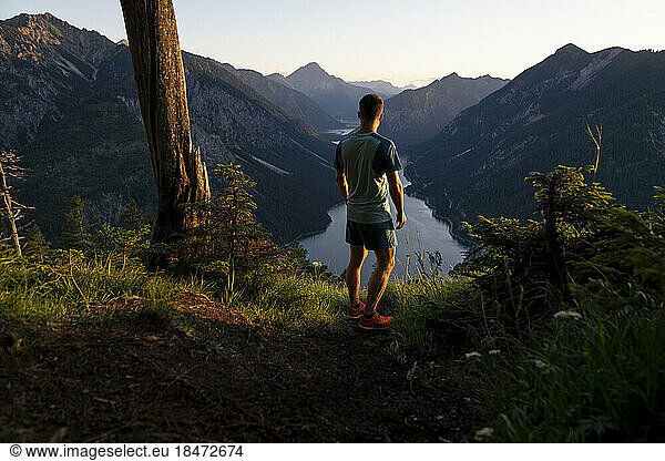 Athlete admiring lake standing on mountain at sunset