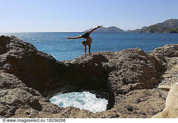 Athlete doing gymnastics on rock by sea