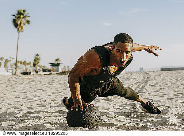 Athlete exercising with medicine ball at beach on sunny day