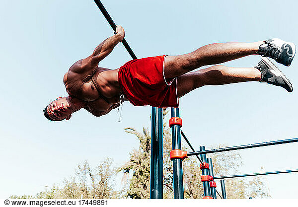 Athlete hanging upside down from a bar in a park.