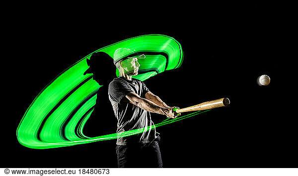 Athlete hitting ball with baseball bat against black background