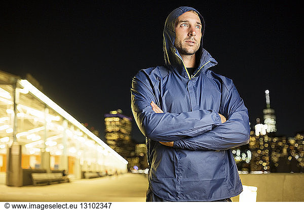 Athlete in hooded jacket standing against illuminated buildings at night