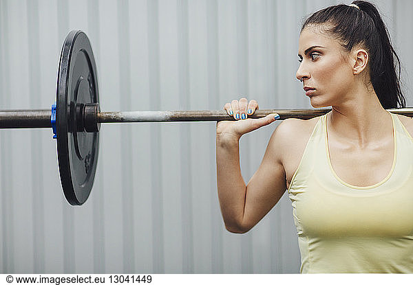Athlete looking away while weightlifting with barbell in gym