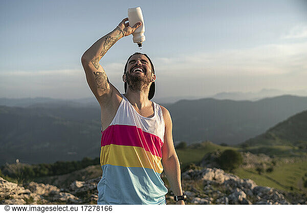 Athlete pouring water on face while standing on mountain against clear sky
